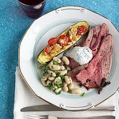 a white plate topped with meat, beans and veggies next to a glass of wine