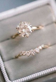 two engagement rings sitting on top of a velvet ring box, one in gold and the other in white