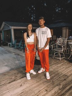 a man and woman standing on a deck in orange sweatpants with writing on them