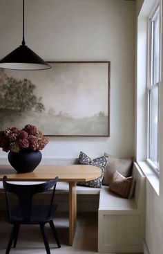 a dining room with a table, bench and painting on the wall above it's windows