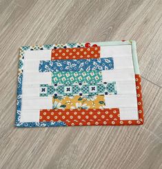 a close up of a piece of fabric on a wooden floor with an orange and blue patchwork design