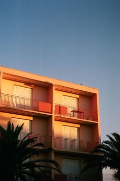 an apartment building with balconies and palm trees in the foreground, against a blue sky