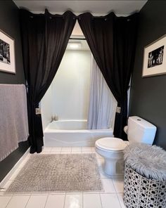 a white toilet sitting next to a bath tub in a bathroom with black curtains on the windows