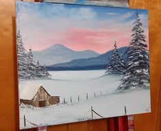 an easel with a painting of a cabin in the snow on it's side