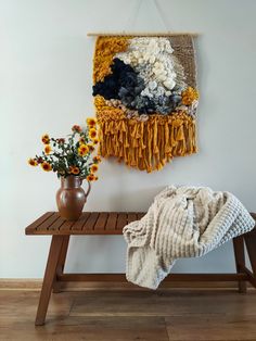 a wooden bench sitting next to a wall hanging with flowers and a blanket on it