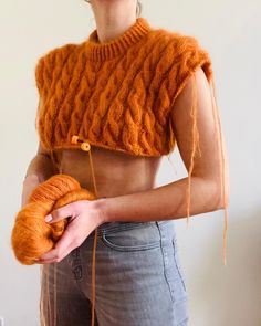 a woman wearing an orange knitted crop top holding a piece of bread in her hands