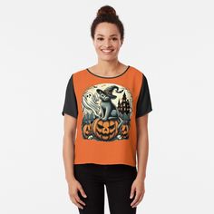 a woman wearing an orange and black top with pumpkins on it, in front of a