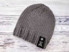 a gray knitted beanie with a black tag on the front and white wood background