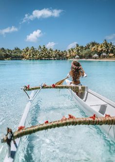 a woman in a white boat on the water with palm trees and blue sky behind her