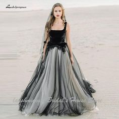 a woman standing on top of a sandy beach wearing a black and grey dress with veil