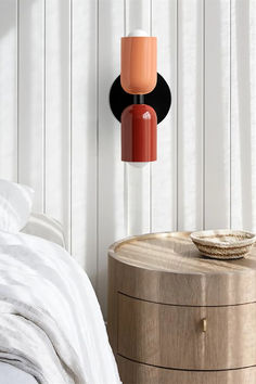 an orange and black lamp hanging from the ceiling next to a round table with a basket on it