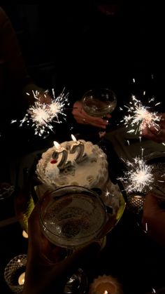 people are holding sparklers over a cake with candles on it and one person is holding a wine glass in front of the cake