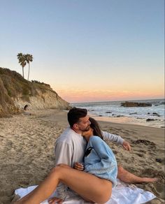 a man and woman sitting on top of a sandy beach