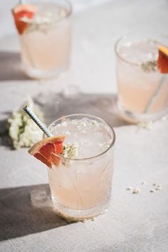 two glasses filled with drinks and garnished with grapefruit on the side