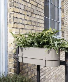 a planter with green plants in it on the side of a brick building next to a window