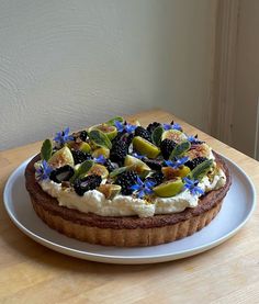 a cake on a white plate with blue flowers and leaves around it, sitting on a wooden table