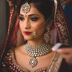 a woman in a red and gold bridal outfit with jewelry on her head looking at the camera