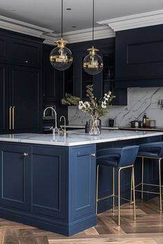 a kitchen with blue cabinets and marble counter tops, gold accents and pendant lights hanging from the ceiling