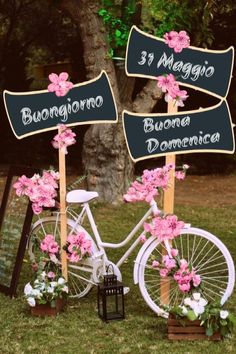 a white bicycle with pink flowers on it parked in front of a sign that says 3 maggios