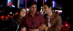 three people sitting on a bench in front of a city street at night with neon lights behind them