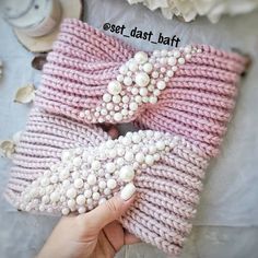 a hand holding a pink and white knitted mitt with pearls on the top