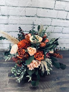 an arrangement of flowers and greenery on a wooden table in front of a brick wall