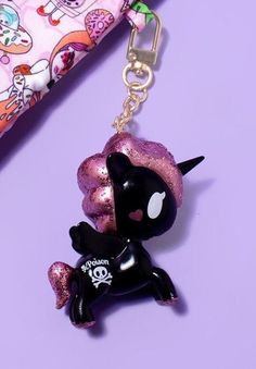 a black and pink keychain with a skull on it's side, sitting next to a purse