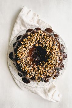 a cake with chocolate frosting and nuts on top sitting on a white tablecloth