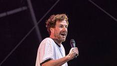 a man holding a microphone in his right hand and making a face while standing on stage