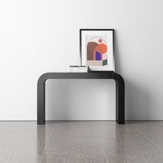 a black table sitting in front of a white wall with a framed painting on it