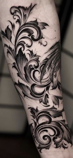 a black and white tattoo design on the left arm, with swirls and leaves