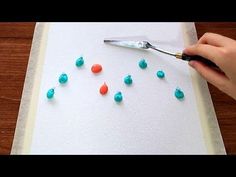 someone is painting small blue and orange balls on a piece of paper with a paintbrush