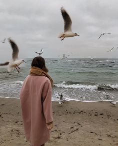 a woman standing on the beach watching seagulls flying over the water and sand