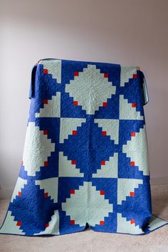 a blue and white quilt with red, white, and blue squares on it sitting on the floor