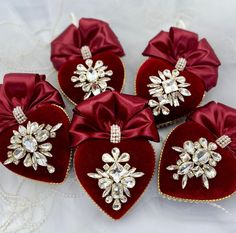 four red velvet heart shaped ornaments with bows and jewels on the top, sitting on a white tablecloth