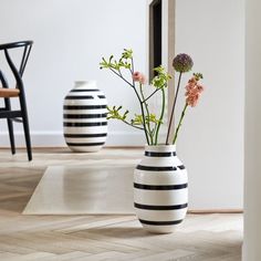 two black and white vases with flowers in them sitting on the floor next to a mirror