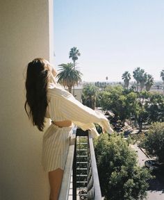 a woman standing on top of a balcony next to a palm tree filled sky line