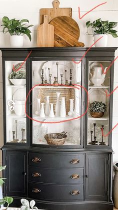 a black china cabinet with lots of plants on top and red arrows pointing to the bottom