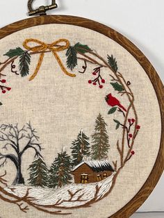 an embroidered christmas wreath with a red bird on it and evergreen trees in the background