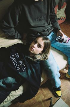 a man and woman sitting on the floor next to each other with guitars in the background