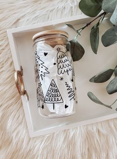 a glass jar with an eagle and christmas tree on it sitting on a tray next to eucalyptus leaves