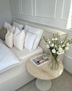 a white couch with pillows and flowers in a vase on the table next to it