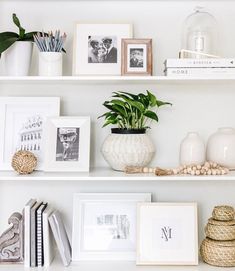 some white shelves with pictures, frames and plants on top of each shelf in front of them