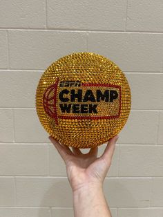 a hand holding up a gold ball with the word champ week written on it