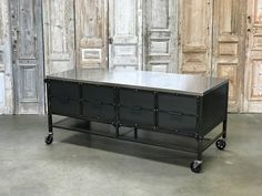 an industrial steel table with four drawers on casteors in front of wood paneled doors