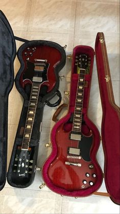 three guitars are laying on the floor next to each other, one is red and one is black