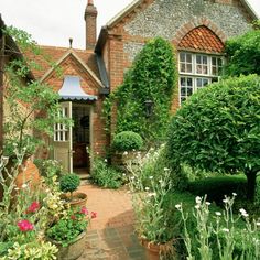 a brick house surrounded by greenery and flowers