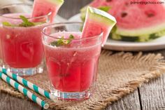 two glasses filled with watermelon drink next to some slices of watermelon