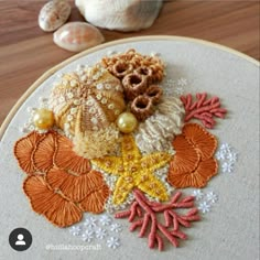 a close up of a embroidery on a wooden surface with shells and seashells in the background