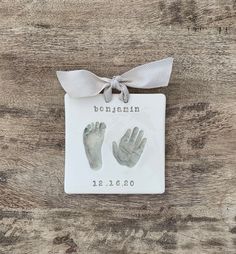 a baby's hand and foot print on a white plaque with a ribbon around it